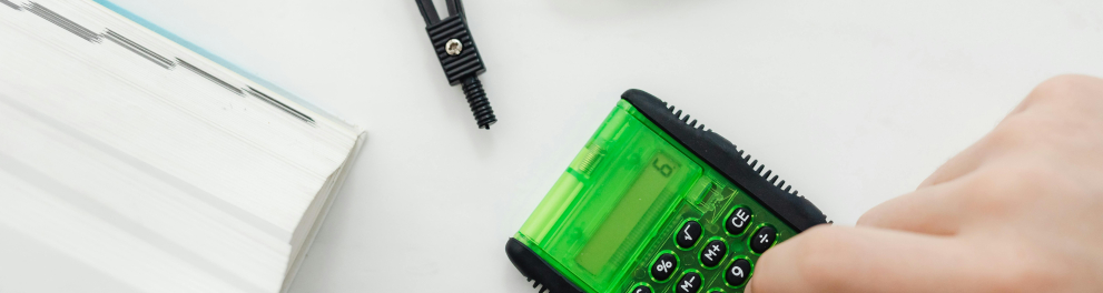 Em uma superfície branca, uma mão digita em uma calculadora verde.