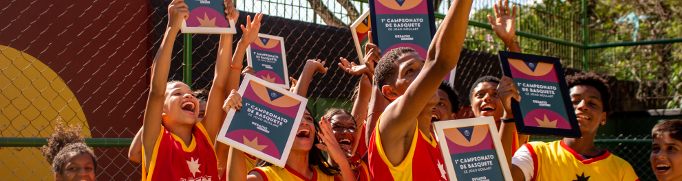 Diversas crianças e jovens seguram certificados com as mãos erguidas.
