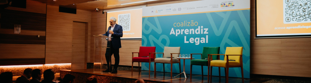 Homem está de pé sobre o palco de um auditório.