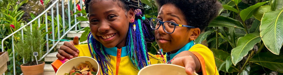 Duas crianças sorriem, segurando folhas coloridas.