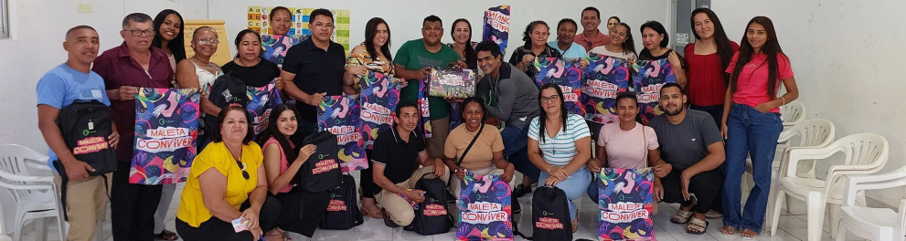 Diversas pessoas, de pé e agachadas, seguram suas Maletas Conviver.