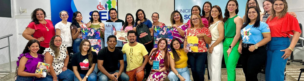 Diversas pessoas de pé e agachadas, sorrindo, em uma sala de aula.