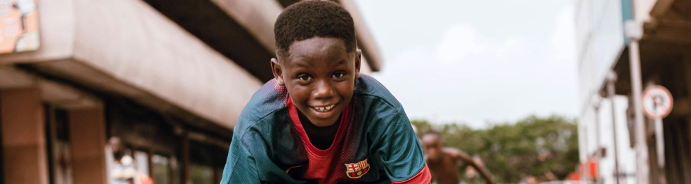 Um menino anda de patins, sorrindo, em uma rua de uma cidade grande.