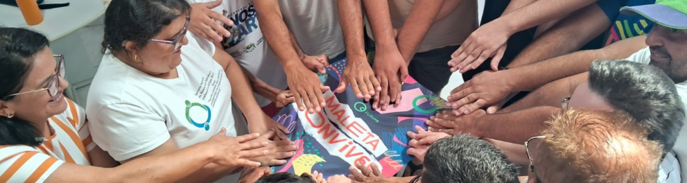 Um grupo de pessoas organizadas em roda e com as mãos estendidas