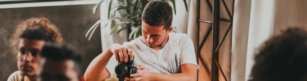 A imagem mostra um jovem tirando fotos com o auxílio de uma câmera fotográfica profissional durante um evento