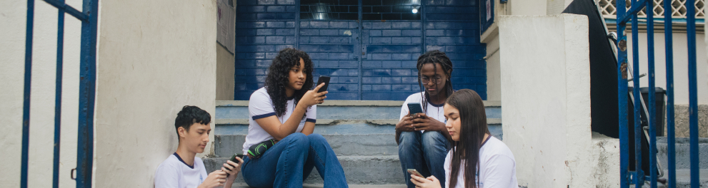 Adolescentes usando celulares na entrada de uma escola