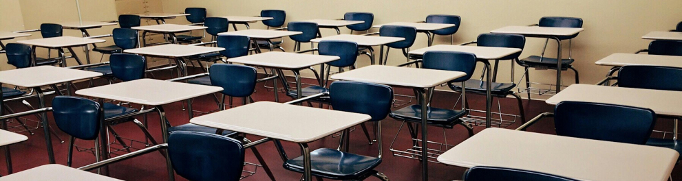 Sala de aula vazia, com muitas mesas e cadeiras escolares.