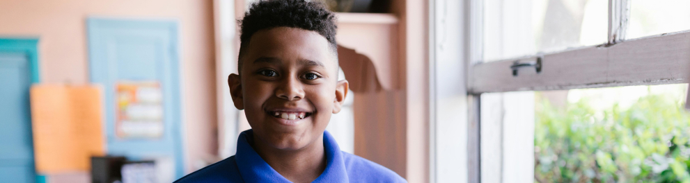 A imagem mostra um menino com um livro aberto em mãos e sorrindo para a foto