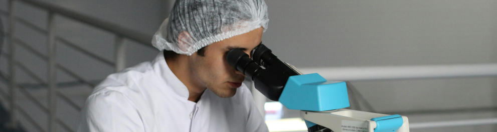 A imagem mostra um homem em um laboratório usando um microscópio. 
