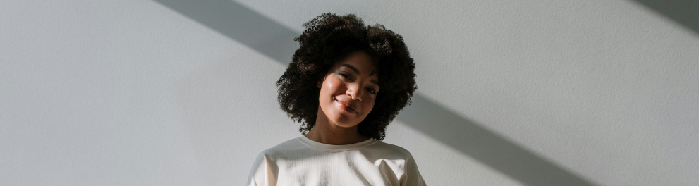 A imagem mostra uma jovem negra grávida, sorrindo e com as mãos na barriga