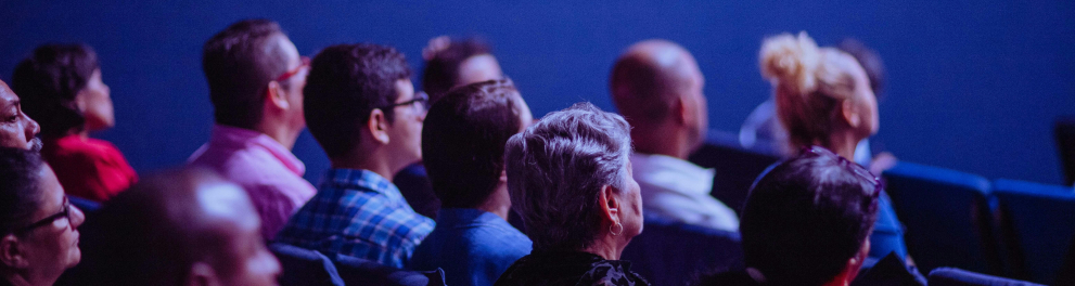 A imagem mostra um grupo de pessoas em uma plateia