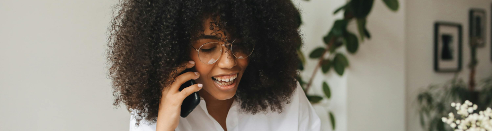 A imagem mostra uma jovem negra falando ao celular e usando um notebook