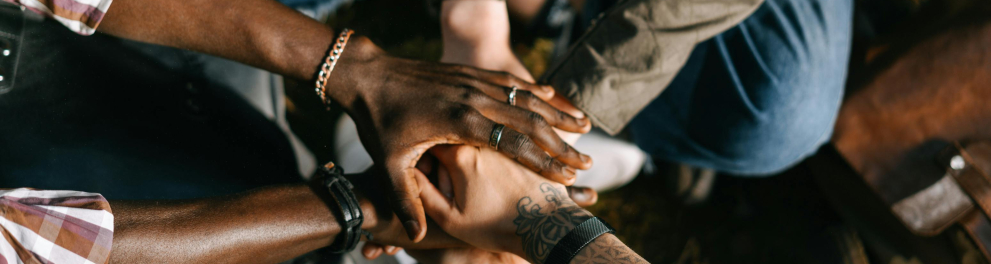 A imagem mostra um grupo de pessoas de diferentes etnias apoiando suas mãos sobre as outras
