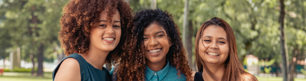 A imagem mostra três jovens abraças e sorrindo para a foto