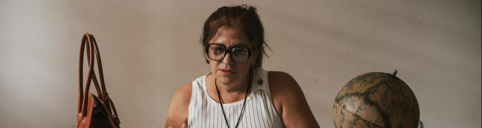 A imagem mostra uma mulher sentada em uma mesa olhando papeis