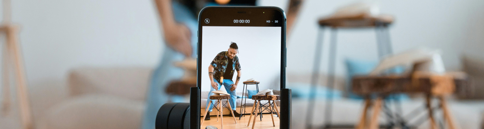 A imagem mostra um rapaz criando conteúdo em um celular com o auxílio de um tripé