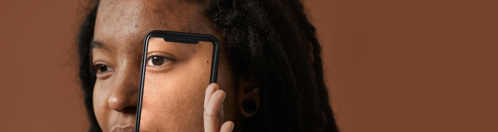 A imagem mostra uma mulher com expressão séria segurando um celular na frente do seu rosto