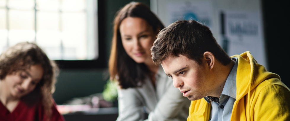 Em primeiro plano, um rapaz, à direita, está observando algo. Ao fundo, duas mulheres o observam.