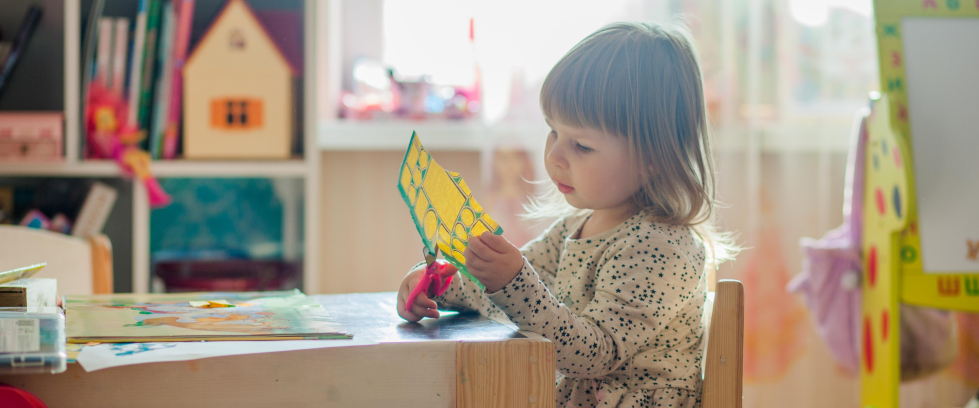 Uma menina com idade em torno de 4 anos recorta um papel.