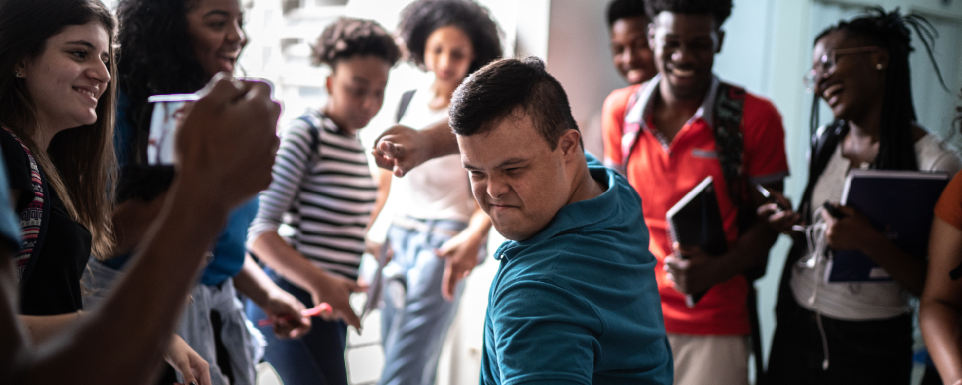 Várias pessoas observam uma outra pessoa, esta, com Síndrome de Down, que parece estar dançando.