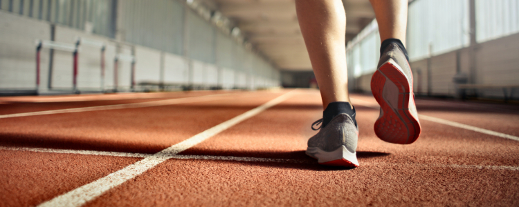 Imagem com uma pista de atletismo, mostrando as pernas de um atleta em vias de dar o promeiro passo.