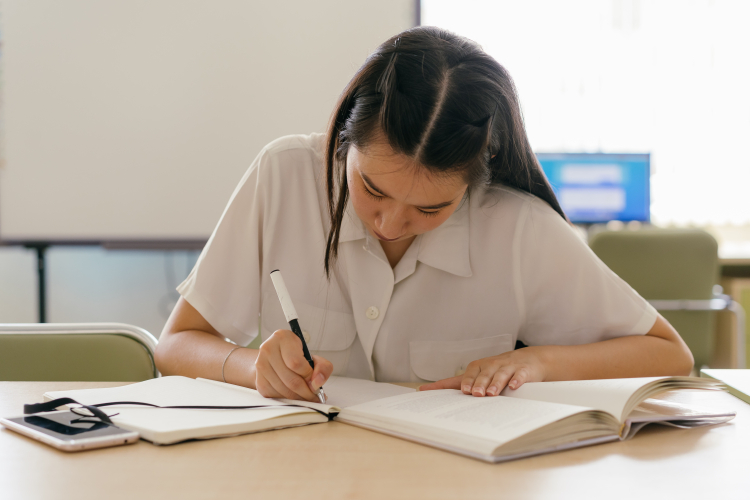 menina escrevendo e com um livro aberto sobre a mesa