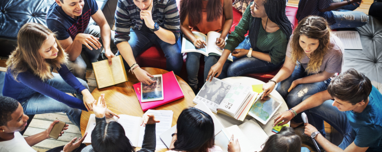 Várias e vários jovens estão sentados ao redor de uma mesa com alguns livros.