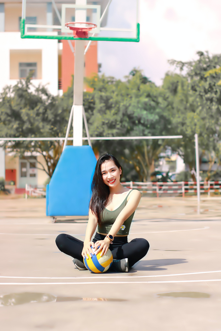 Imagem mostra uma mulher sentada, sorrindo, segurando uma bola de vôlei