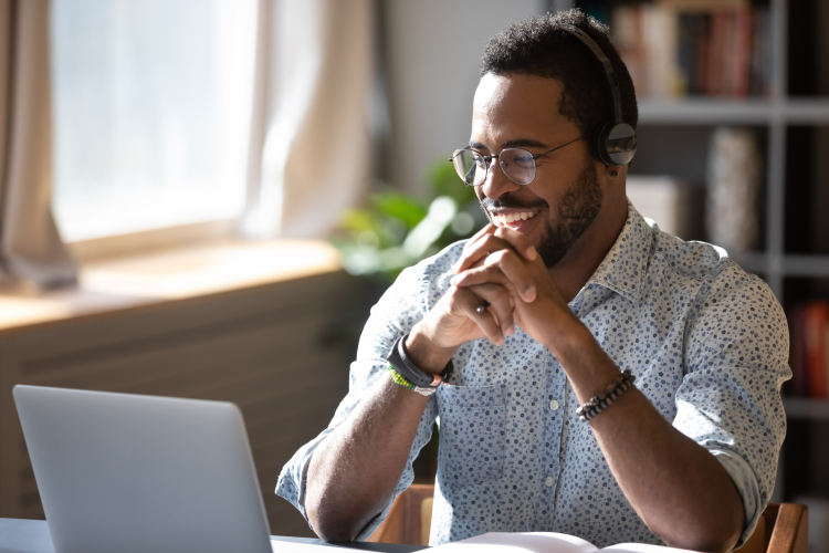 Um homem negro sorri diante de um laptop.