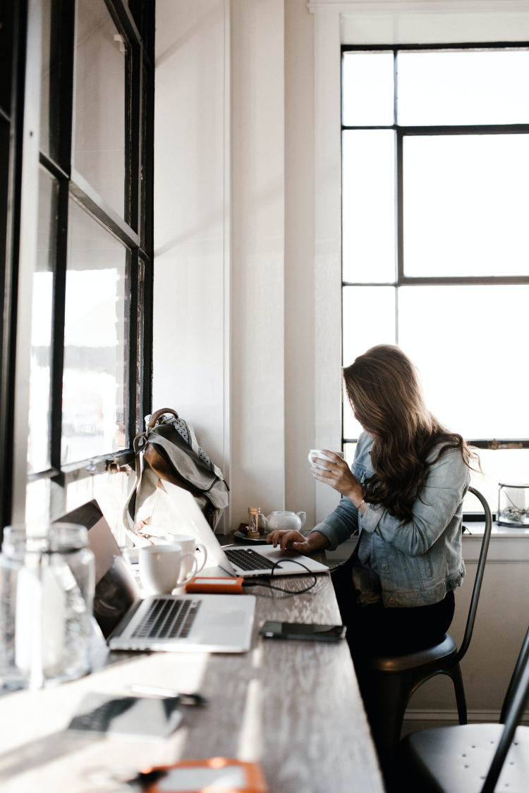 Imagem mostra uma mulher segurando uma xícara e com a outra mão sobre um notebook