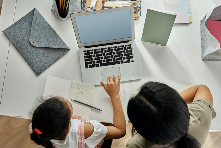 Imagem mostra uma mulher e uma garota em frente a um notebook