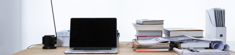 Uma mesa com notebook, luminária, vários livros, canetas...é uma mesa de trabalho e estudos claramente