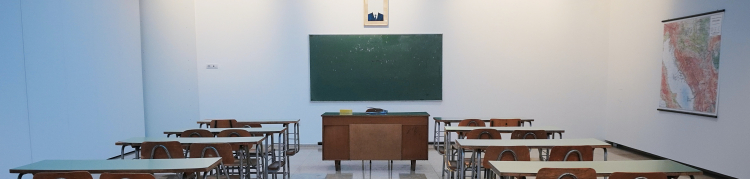 Uma sala de aula vazia, apenas com as cadeiras, a mesa do professor e o quadro negro em branco ao fundo