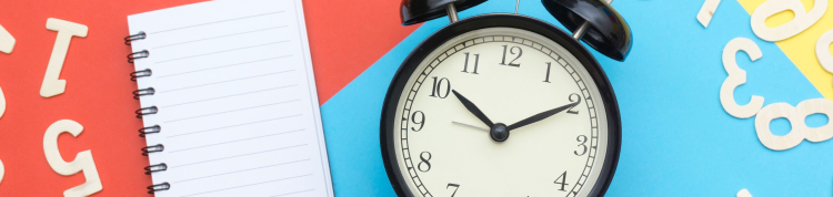 A imagem mostra um caderno, um relógio e vários números em cima de uma superfície vermelha, azul e amarela