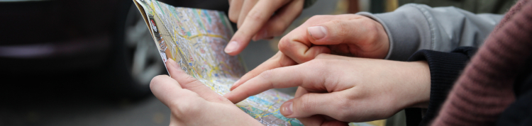 Duas pessoas segurando um mapa de papel e apontando para ele com seus indicadores