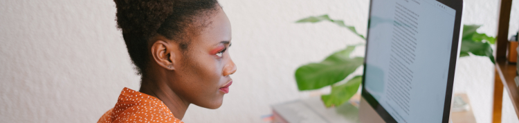Uma mulher negra está escrevendo diante da tela de um computador de mesa.