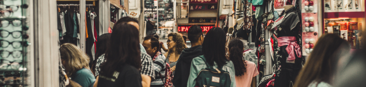 Foto do que parece ser o interior de uma galeria ou shopping, onde há várias pessoas e lojas com placas
