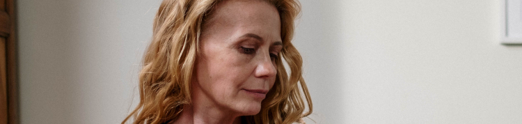 Uma mulher loira está sentada passando, em sua roupa, um rolinho que remove pêlos das roupas p