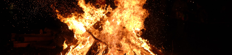 Uma fogueira com bastante gravetos e madeira em sua base e uma labareda alta de fogo à noite