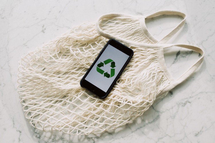 Um celular com a tela mostrando o símbolo verde da sustentabilidade está em cima de uma sacola de lã branca
