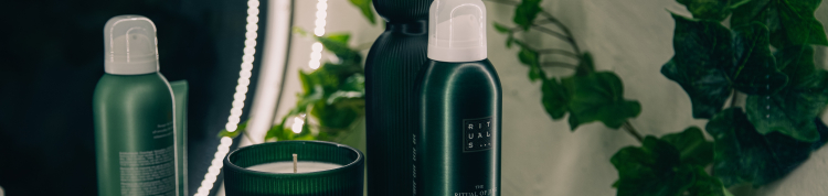 Cosméticos de embalagens verdes estão em cima de uma pia de banheiro com plantas ao lado