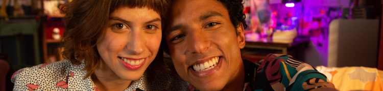 Uma mulher e um homem estão sentados em um sofá. Ambos sorriem.