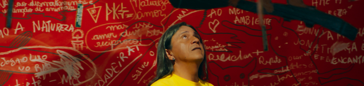 Um homem indígena posando para uma foto na frente de um mural