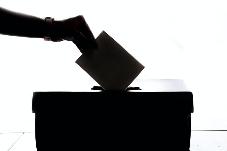 Uma mão depositando um voto em uma urna.