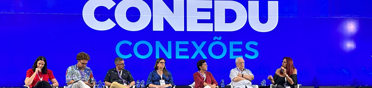Sete pessoas sentadas em cadeiras sobre um palco. Ao fundo, uma projeção azul com o texto "Conedu conexões" em branco.