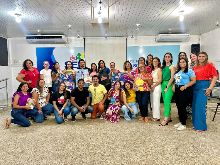Diversas pessoas de pé e agachadas, sorrindo, em uma sala de aula.