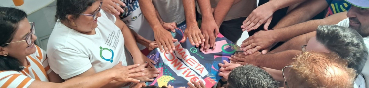 Um grupo de pessoas organizadas em roda e com as mãos estendidas