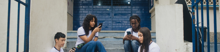Adolescentes usando celulares na entrada de uma escola