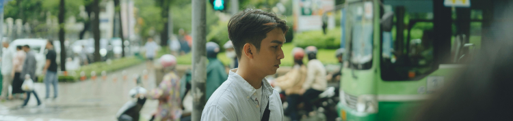 A imagem mostra um jovem andando na calçada de uma rua em um centro urbano