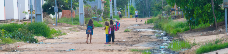 Ao longe, as crianças vão a pé para a escola em uma rua não asfaltada e com esgotão a céu aberto